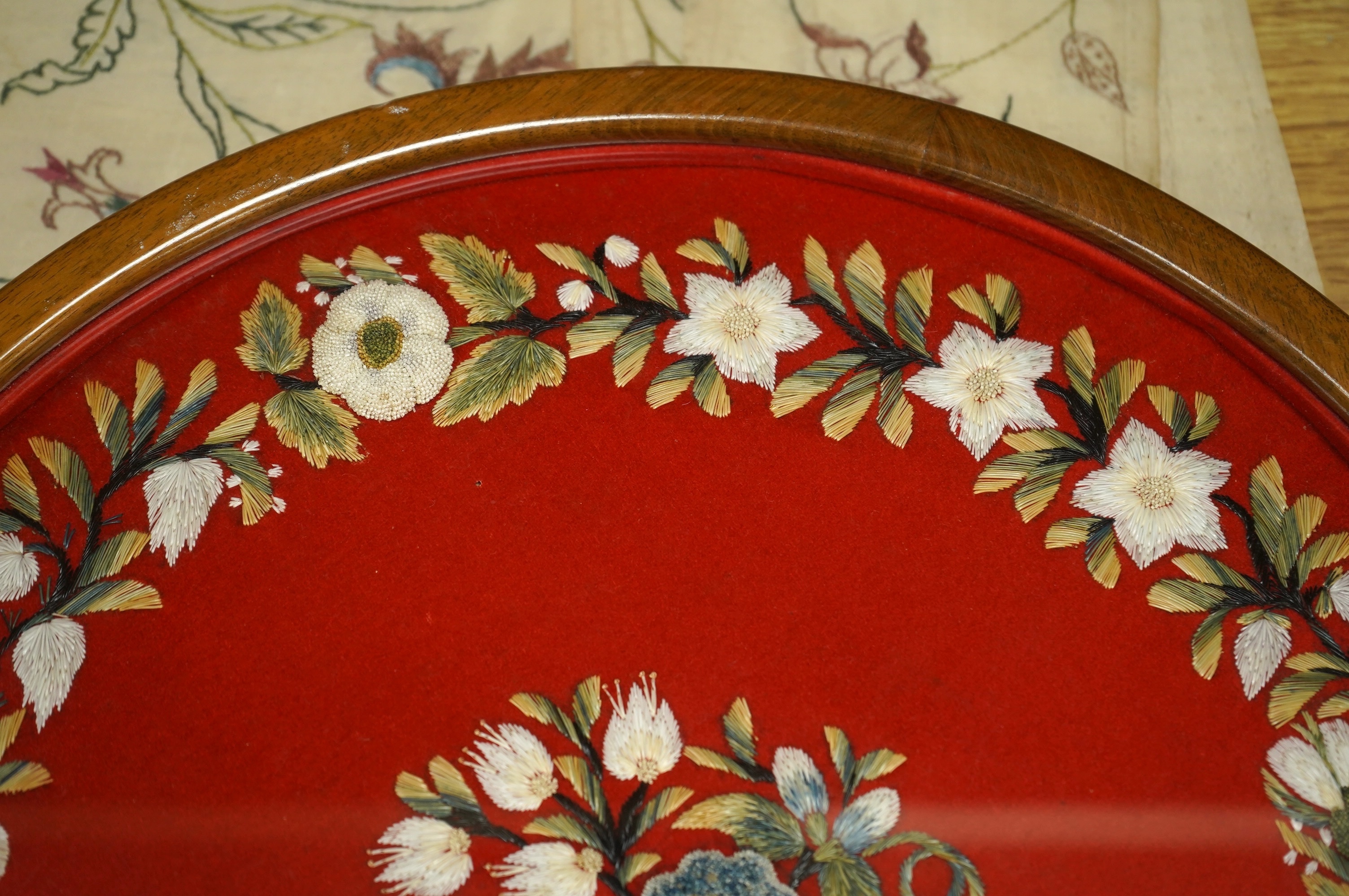 A framed, 19th century, possibly Scandinavian, red felt circular multi-coloured silk embroidery of flowers, acorns and leaves, also embroidered with fine stump work style beadwork flower detail, 32cm diameter. Condition